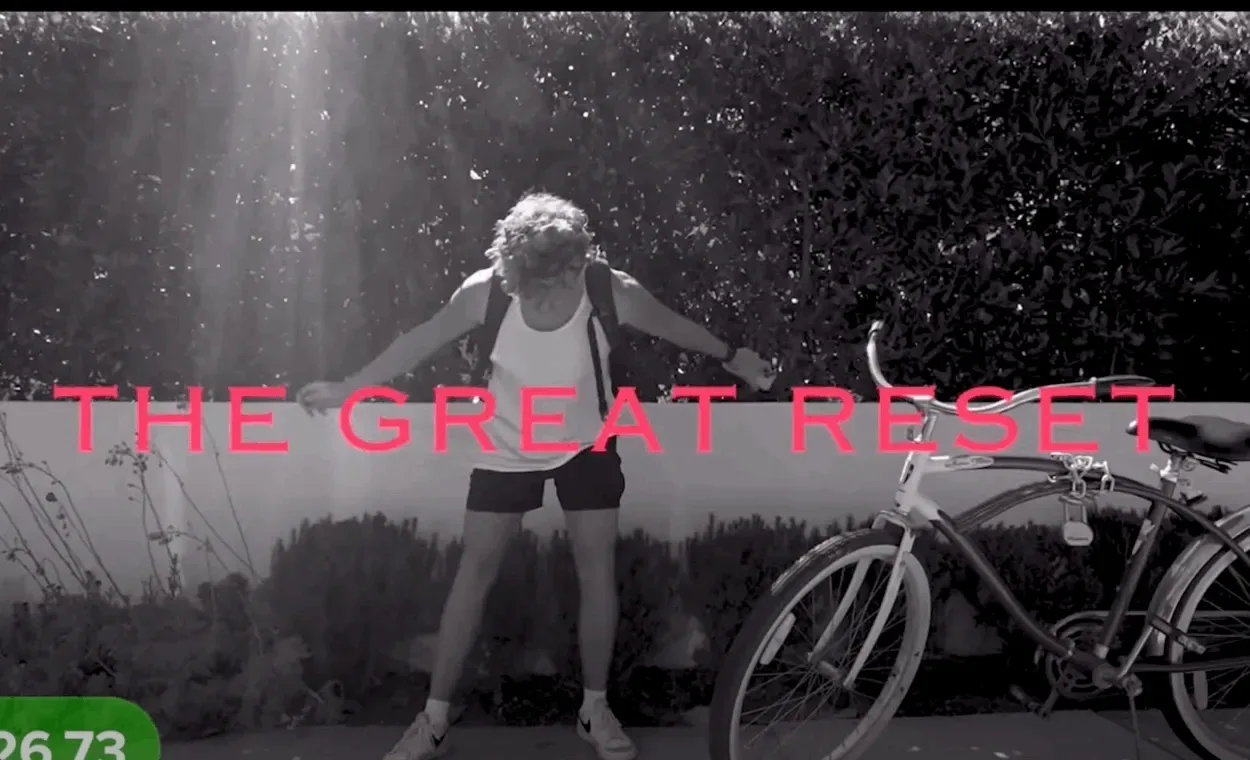 Black-and-white video frame of a man in a tank top dancing beside a bicycle under the pink title 'The Great Reset'.